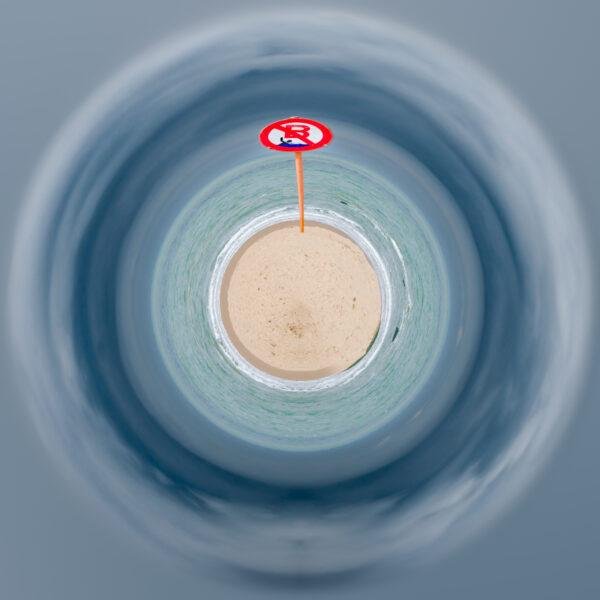 Photo mini planète d'un plage de sable avec un panneau d'interdiction de baignade. La plage est entourée d'eau et l'eau est entourée par le ciel