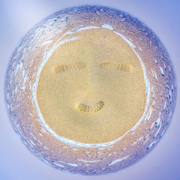 Photo mini planète d'une plage avec un smiley sur le sable, smiley composé de trois empreintes de chaussures
